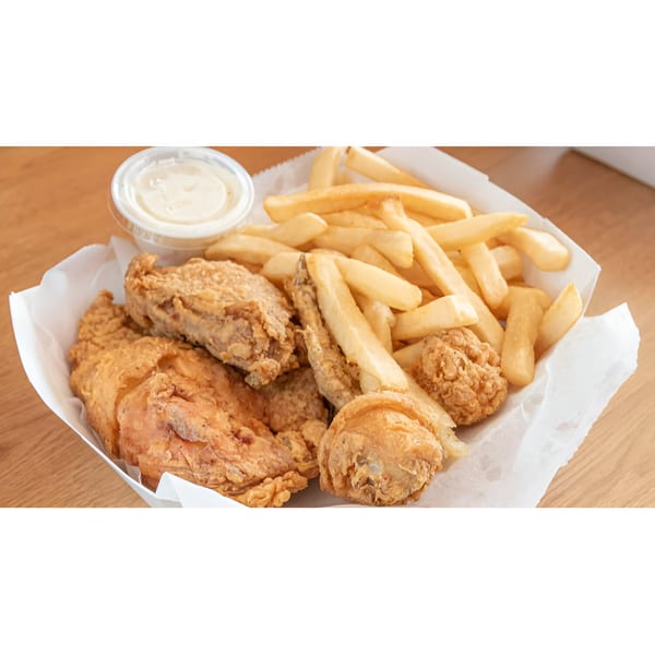 A white paper tray filled with golden-brown fried chicken pieces, french fries, and a side of dipping sauce.