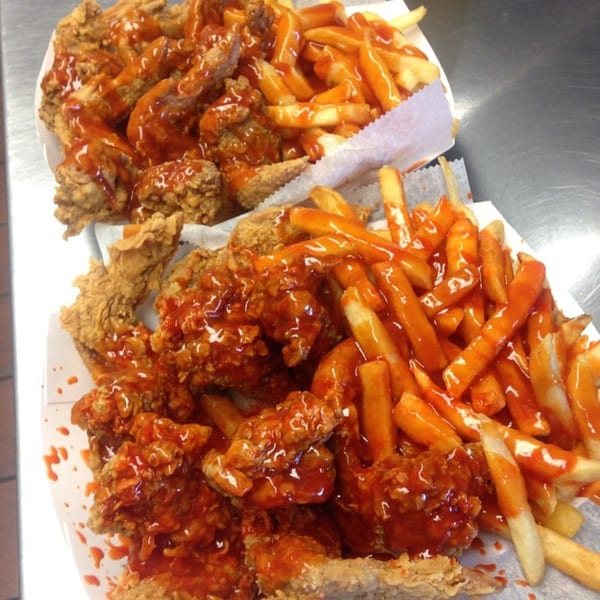 Two servings of Harold's fried chicken and fries, generously drizzled with hot sauce.