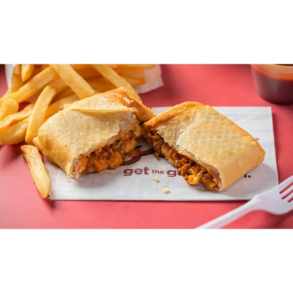 A golden-brown fried chicken burrito, cut in half to show the filling, with french fries.