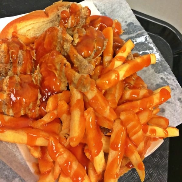 Harold's Chicken Shack fried chicken and fries drenched in bright orange mild sauce, served on white paper.