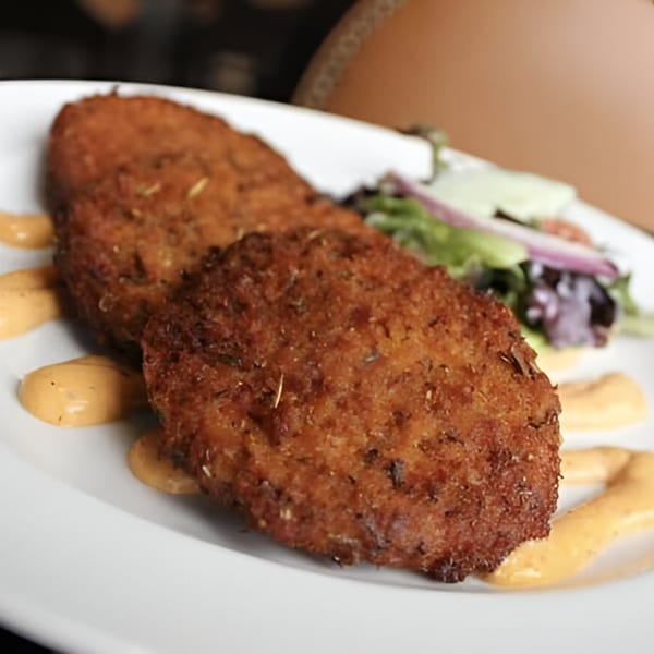 Two crispy fried crab cakes with a side salad and creamy sauce on a white plate.